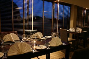 A dining table set for a meal with chairs, a candle, and wine glasses. - Garner Hotel Eight Acres Elgin by IHG (Elgin)