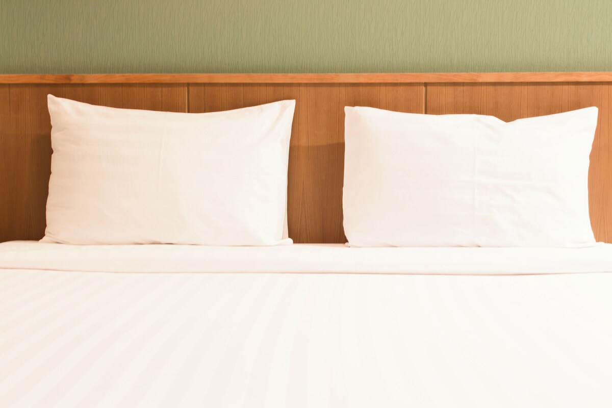 Ein Bett mit zwei Kissen und einem Holz-Kopfstück an einer grünen Wand.