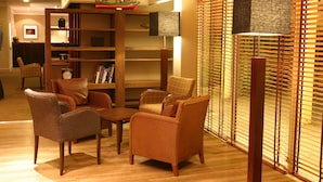 A room with wicker furniture, a bookshelf, and a window with blinds.