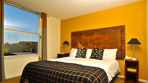 A hotel room with a large bed, two bedside tables, a headboard, and a window with curtains.
