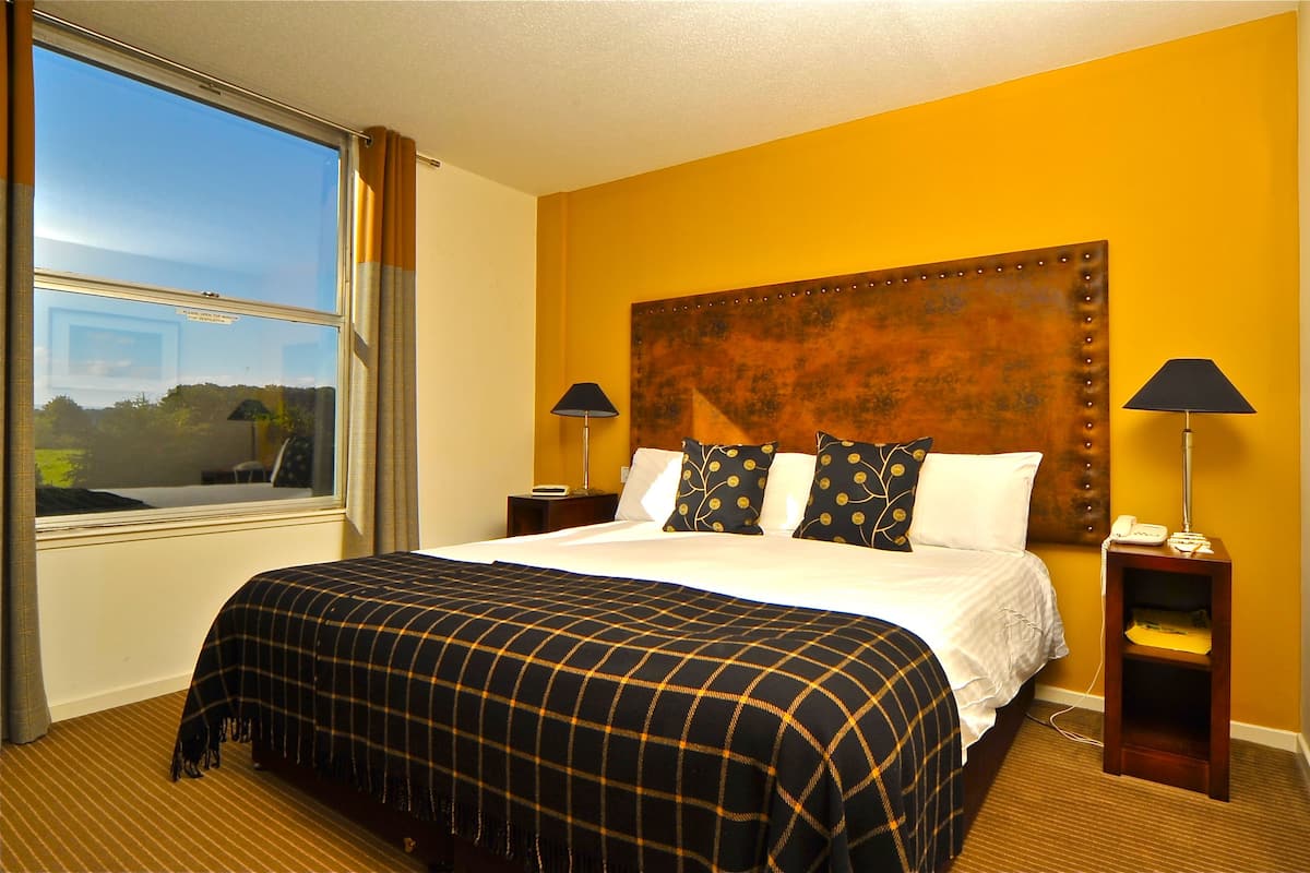 Ein Hotelzimmer mit einem großen Bett, zwei Nachttischen, einer Kopfteil und einem Fenster mit Vorhängen.