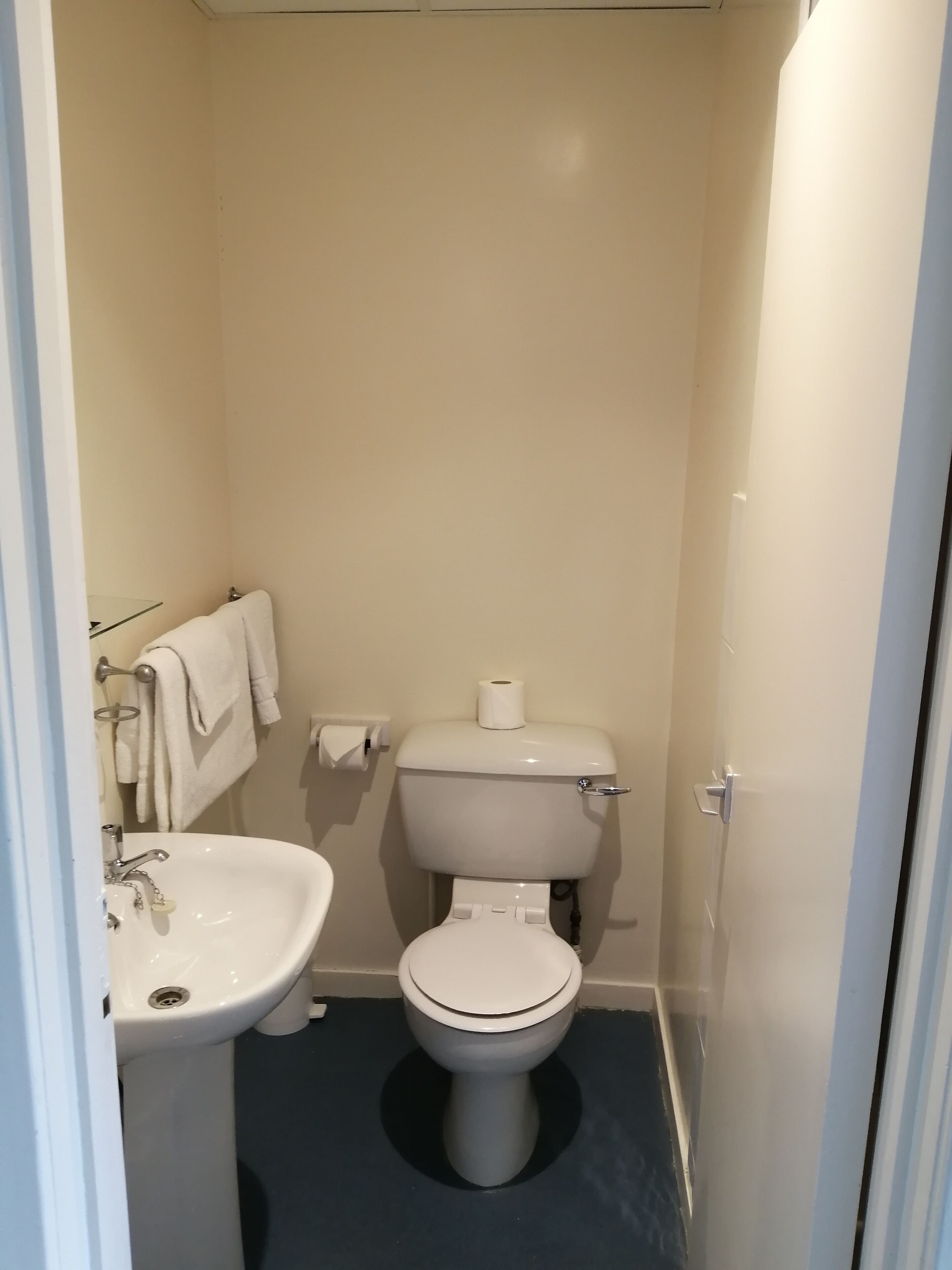 Un baño pequeño y estrecho con un inodoro blanco, un lavamanos blanco y un perchero para toallas.