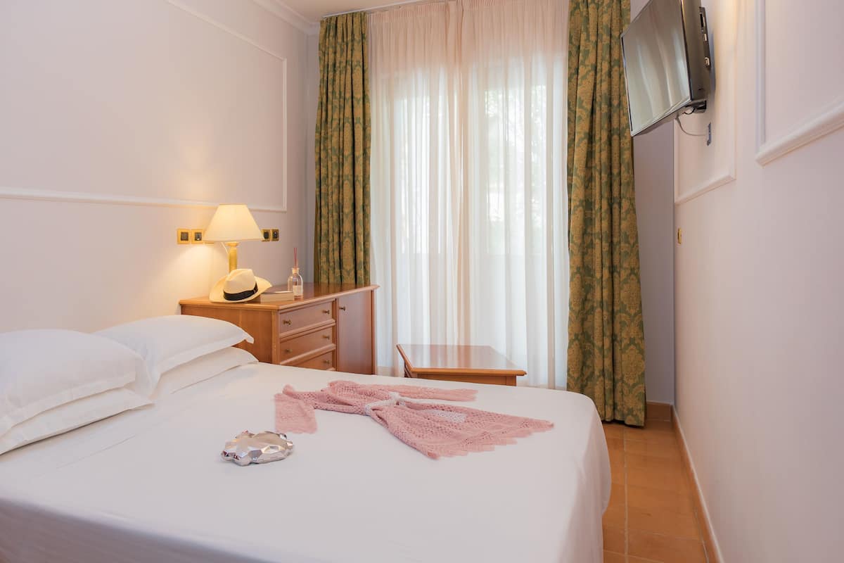 A hotel room with a bed, a bedside table with a lamp, a TV mounted on the wall, and curtains.