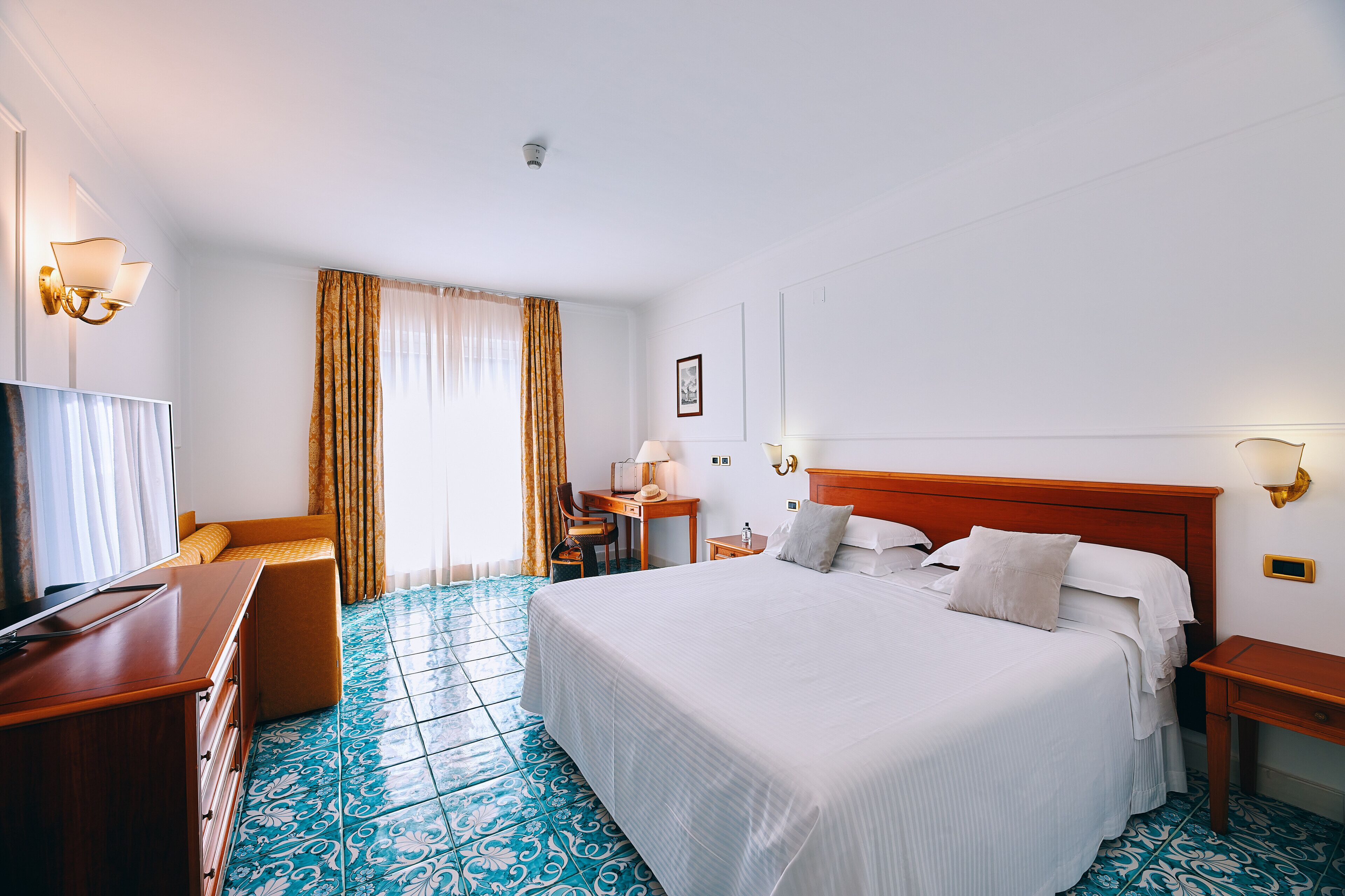 A hotel room with a large bed, a desk with a chair, a TV, and a window with curtains.