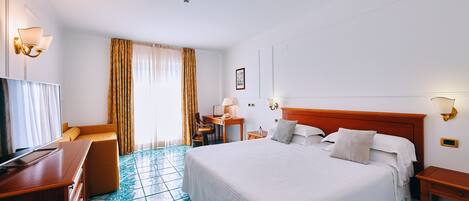 A hotel room with a large bed, a desk with a chair, a TV, and a window with curtains.