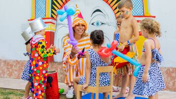 Crianças brincando com balões e um palhaço em um ambiente externo colorido.