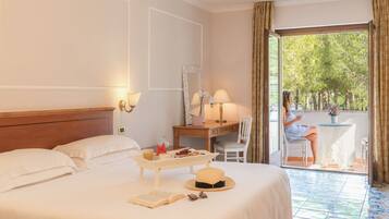 A hotel room with a bed, bedside table, desk, chair, and a balcony with a view of trees.