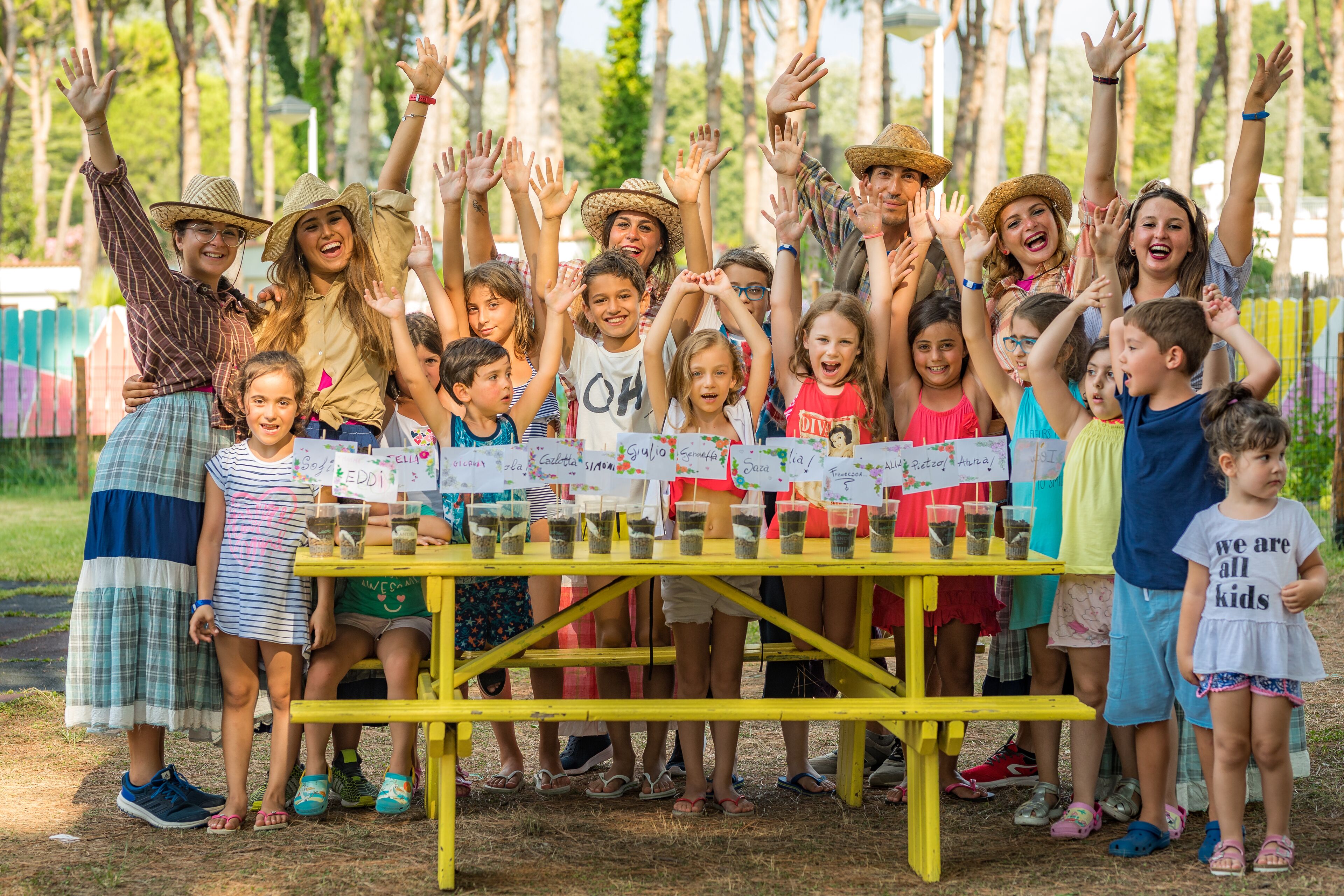 Un groupe d’enfants se tient devant une table sur laquelle sont disposés des gobelets étiquetés, et ils participent peut-être à une expérience ou à une activité scientifique.