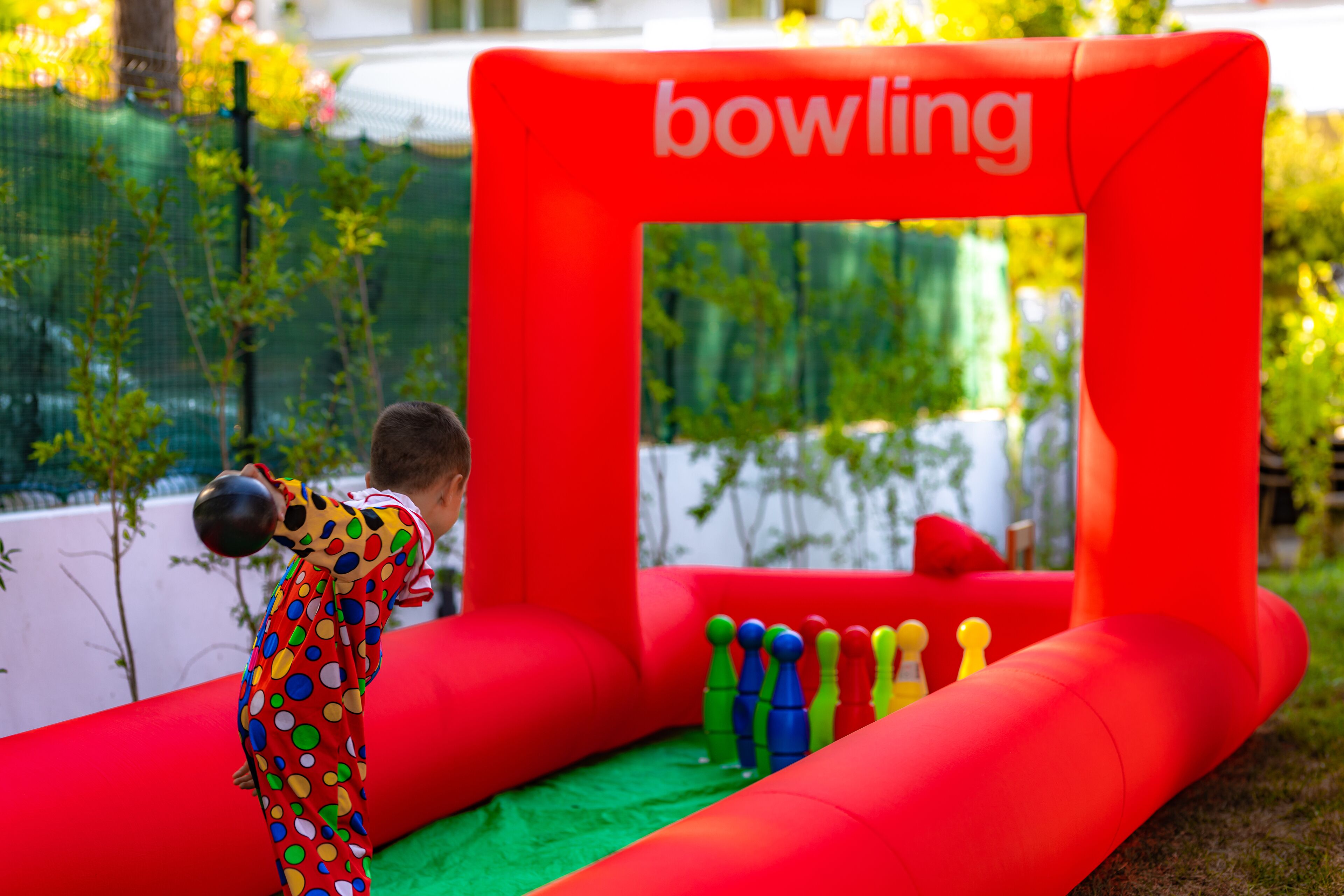 Een kind speelt in een rode opblaasbare bowlingbaan, met een bord waarop 'bowling' staat.