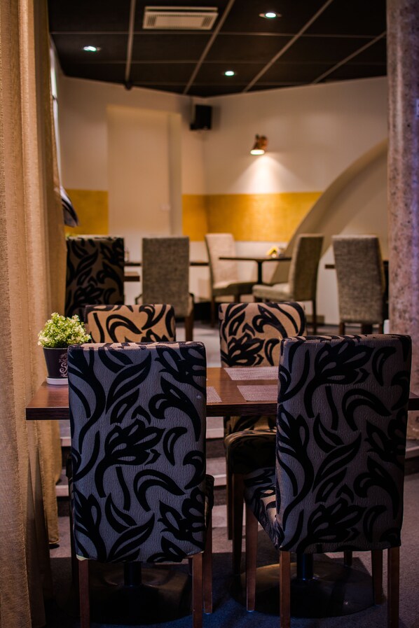A dining area with patterned chairs and a table, a potted plant, and a yellow accent wall. - Braavo Spa Hotel (Tallinn)