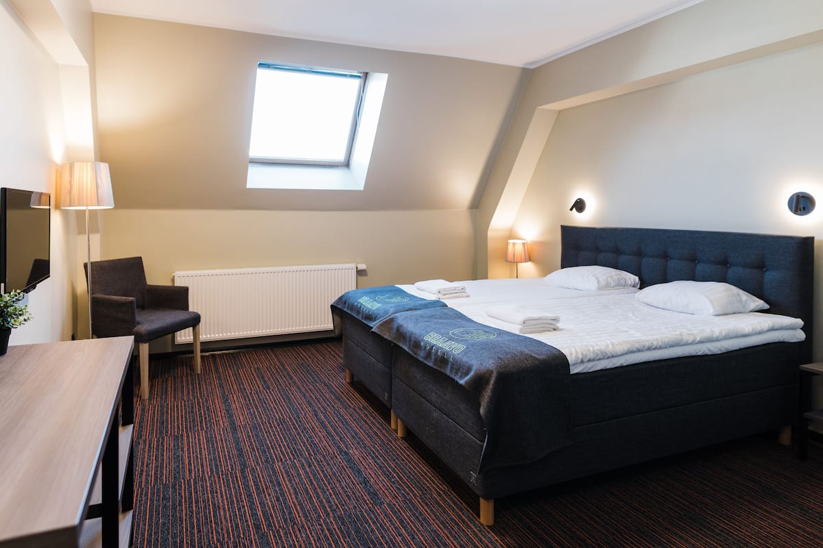 Ein Hotelzimmer mit einem Bett, einem Schreibtisch, einem Sessel, einem Heizkörper, einem Fenster und zwei Wandleuchten.