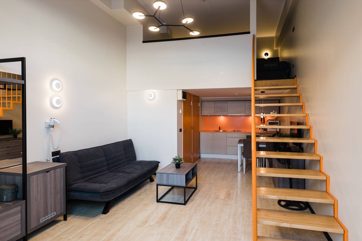 Ein moderner Wohnraum mit Sofa, einem kleinen Tisch, einer Treppe und einer Küchenzeile.