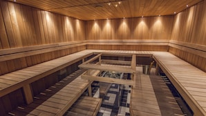 A sauna with wooden walls and benches, a central heating element, and a checkered floor. - Braavo Spa Hotel (Tallinn)