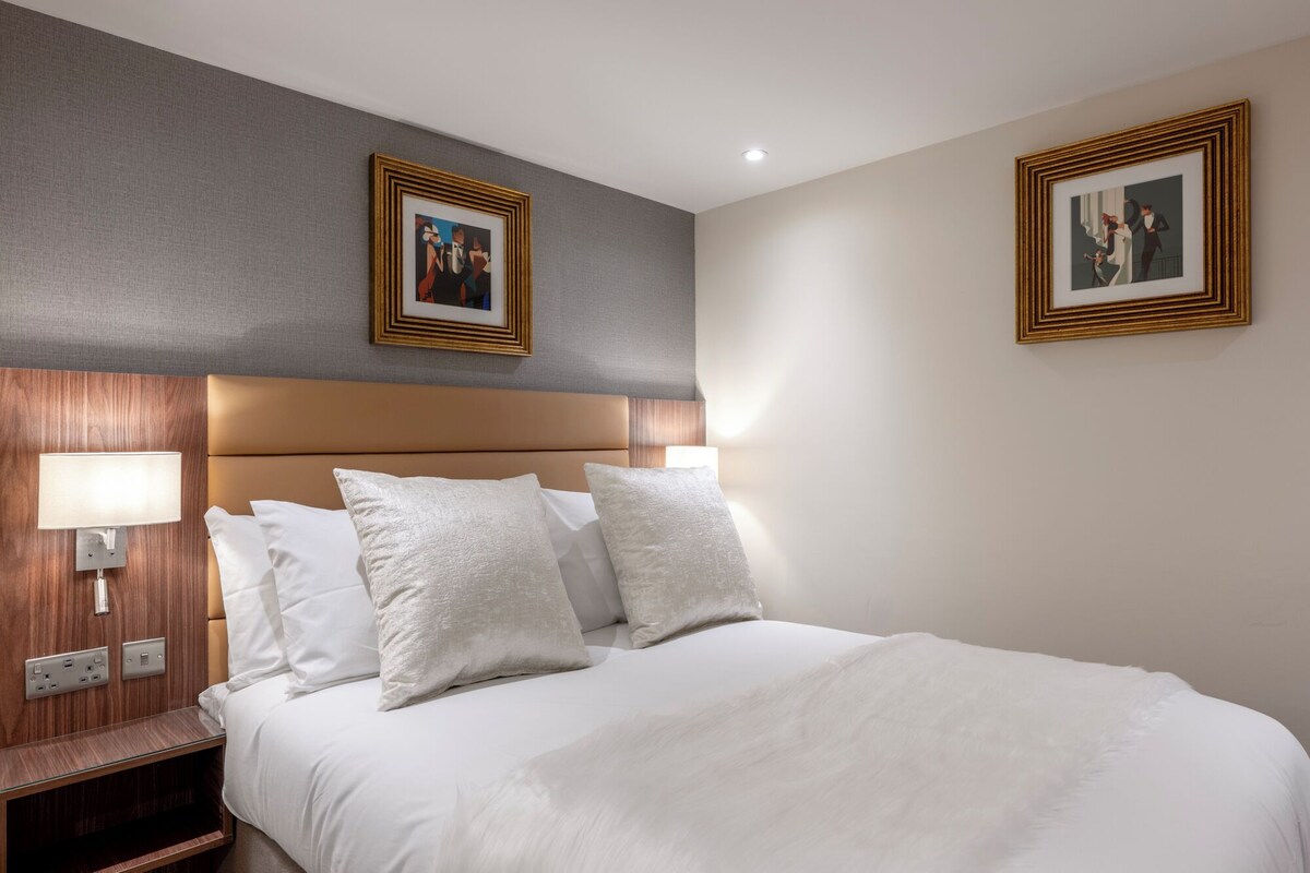 Una habitació d'hotel amb un llit gran, dues làmpades penjades a la paret i dos quadres emmarcats a les parets.