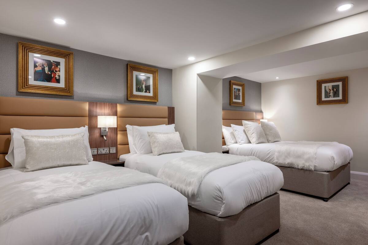 A hotel room with three beds, a large mirror, and framed pictures on the walls.