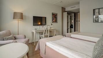A hotel room with a bed, a desk with a chair, a TV, a lamp, and a wardrobe.
