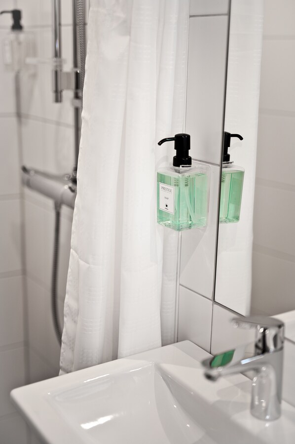 Un baño con lavamanos blanco, un espejo y una ducha con cortina blanca.