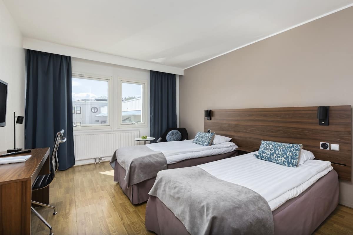 Une chambre d’hôtel avec deux lits, un bureau, une chaise, une télévision et une fenêtre avec des rideaux.