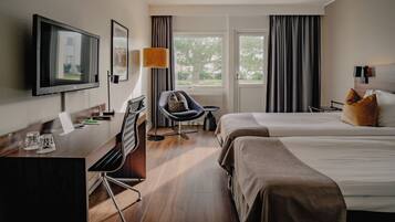 A hotel room with a bed, a desk with a chair, a television, and a window with curtains.