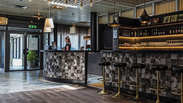A modern bar area with a stone counter, bar stools, and a variety of bottles and glasses. - Apple Hotel (Gothenburg)