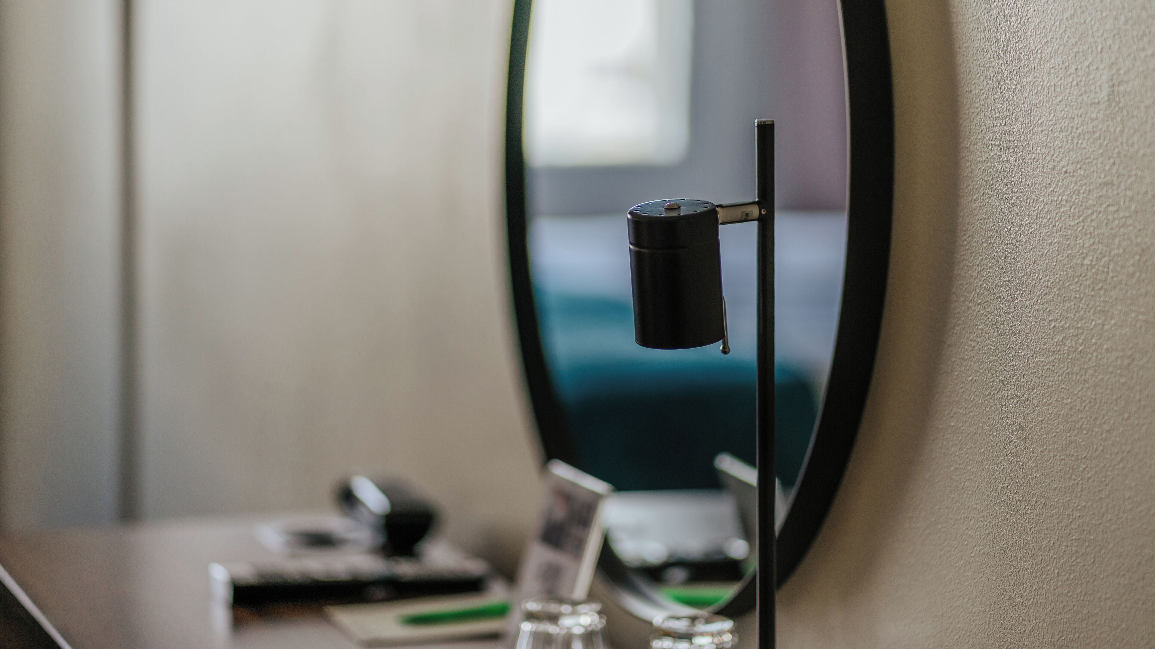 Une pièce avec un miroir rond, une petite table sur laquelle se trouvent une télécommande, un verre et un objet vert.