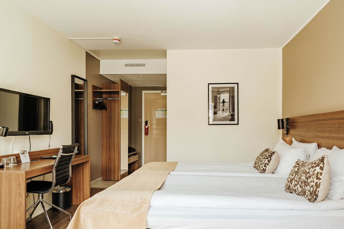 Une chambre d’hôtel comprenant un lit, un bureau avec une chaise, une télévision et une porte donnant accès à une salle de bain.
