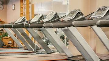 A row of stationary exercise bikes with digital displays, in a room with a mirror and a clock on the wall.