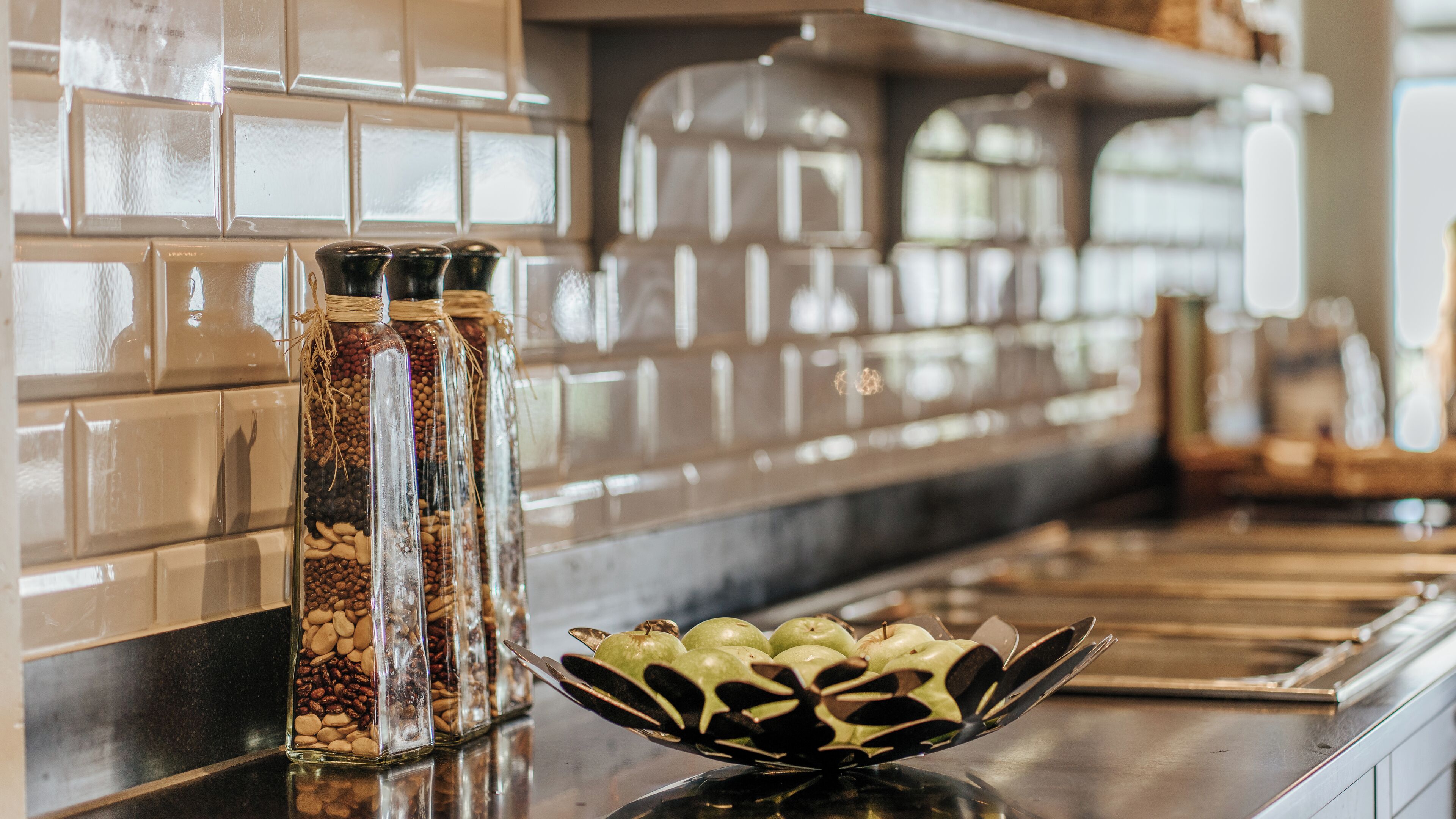 Una cocina con un tarro de vidrio lleno de nueces y un tazón decorativo de manzanas en la encimera.