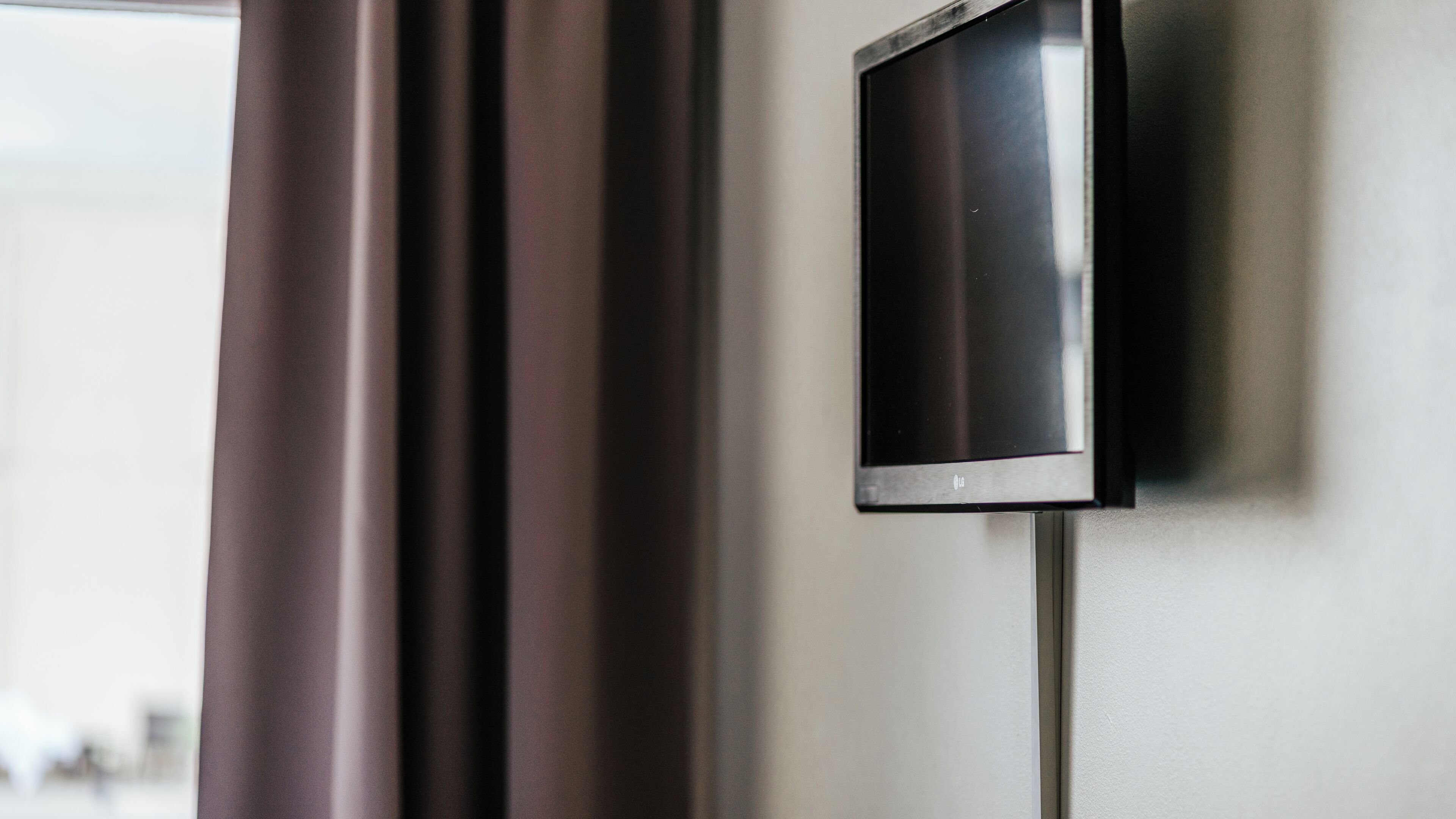 A flat-screen TV mounted on a wall, a curtain, and a partial view of a room.