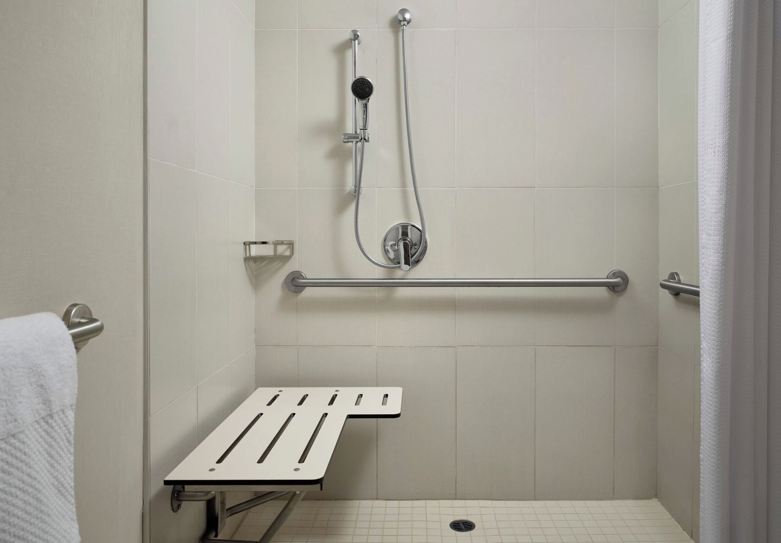 A shower area with a grab bar, a handheld showerhead, and a white towel.