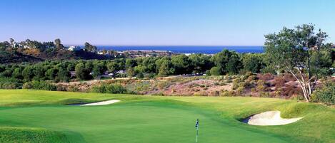 A golf course with a clear view of the ocean and residential buildings in the background.