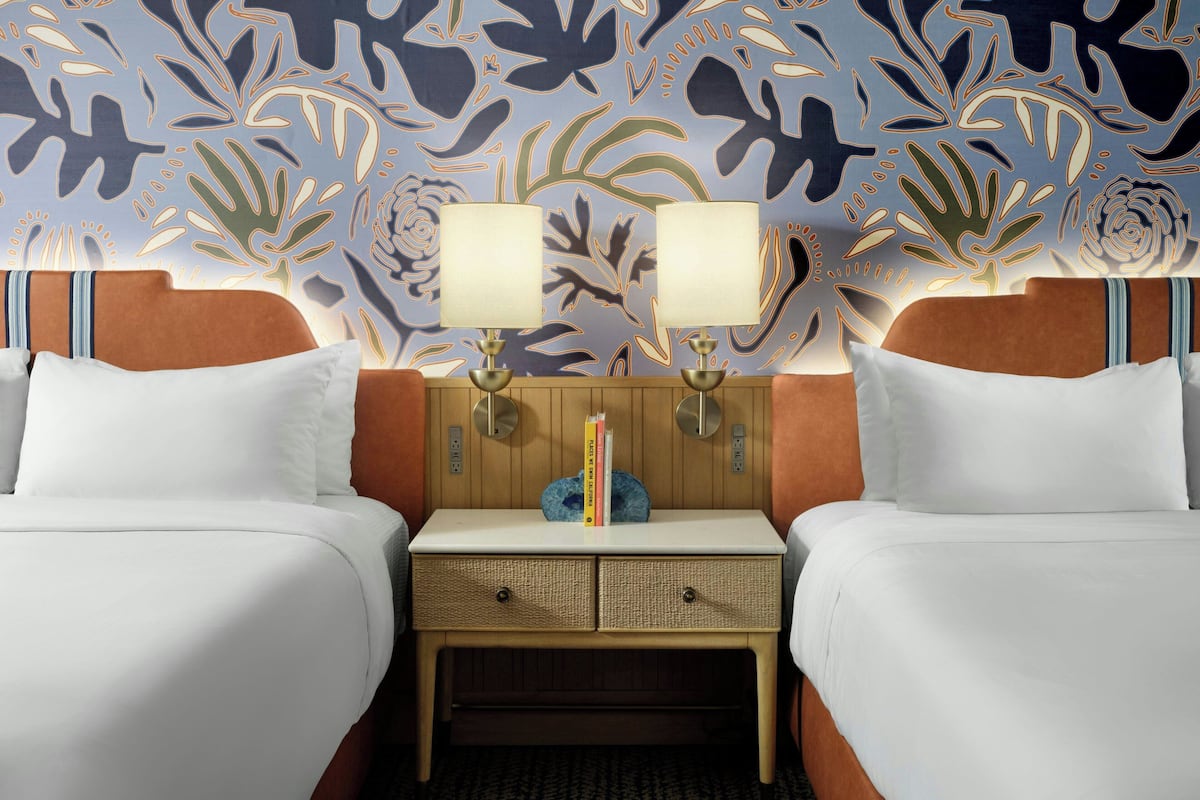 Ein Hotelzimmer mit zwei Betten, einem Nachttisch mit Lampen und einer Wand mit Blumenmuster.