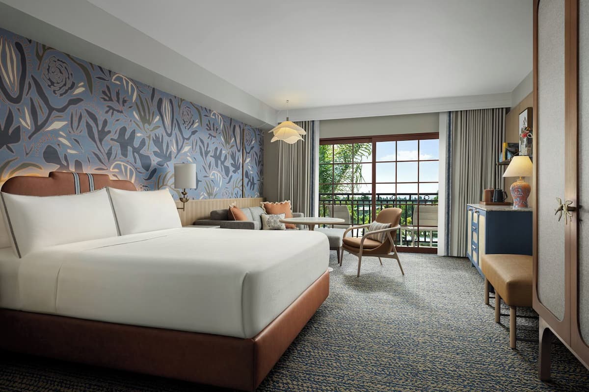 Ein Hotelzimmer mit einem großen Bett, einem Schreibtisch, einem Stuhl, einem kleinen Tisch, einer Lampe und Blick ins Freie.