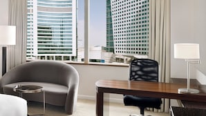 Habitación de hotel moderna con un gran ventanal que ofrece vistas a la ciudad, una mesa redonda, un sofá y una silla.