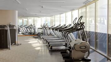 Un gimnasio con múltiples cintas de correr alineadas en filas, ventanas amplias y un diseño moderno y limpio.