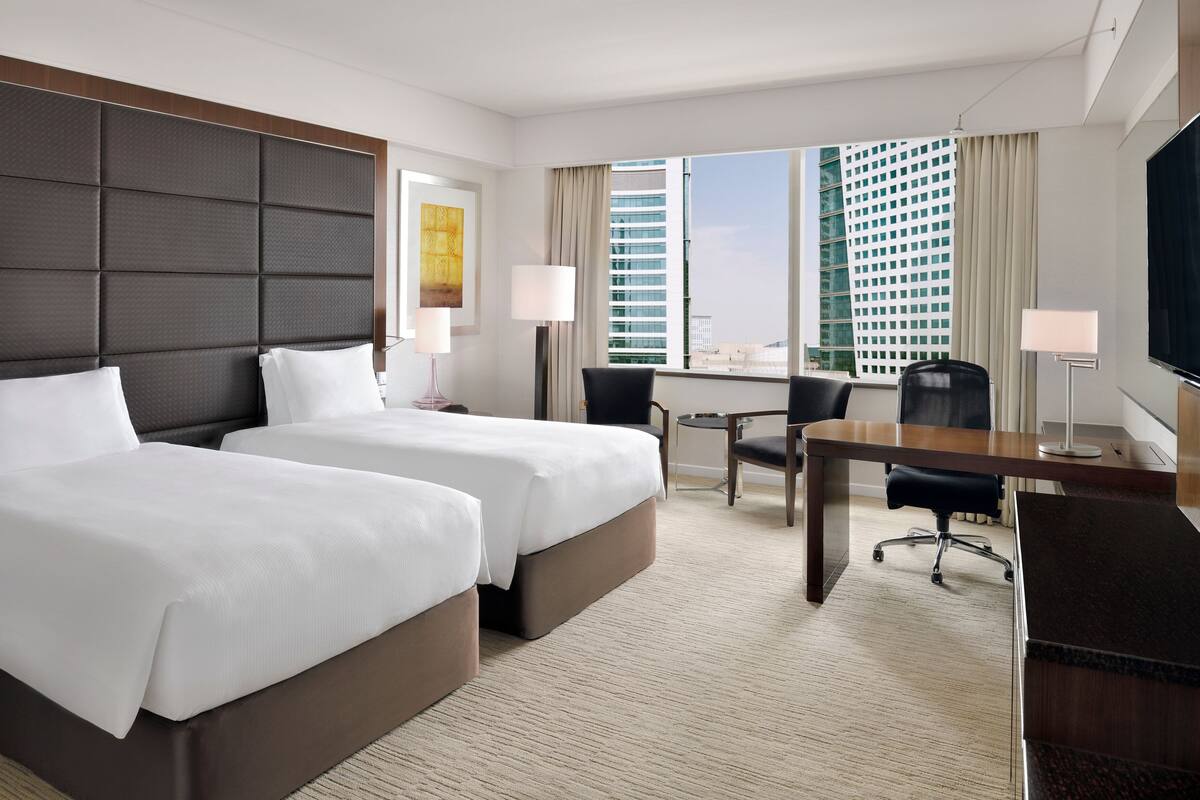 A hotel room with two beds, a desk, a chair, and a TV.