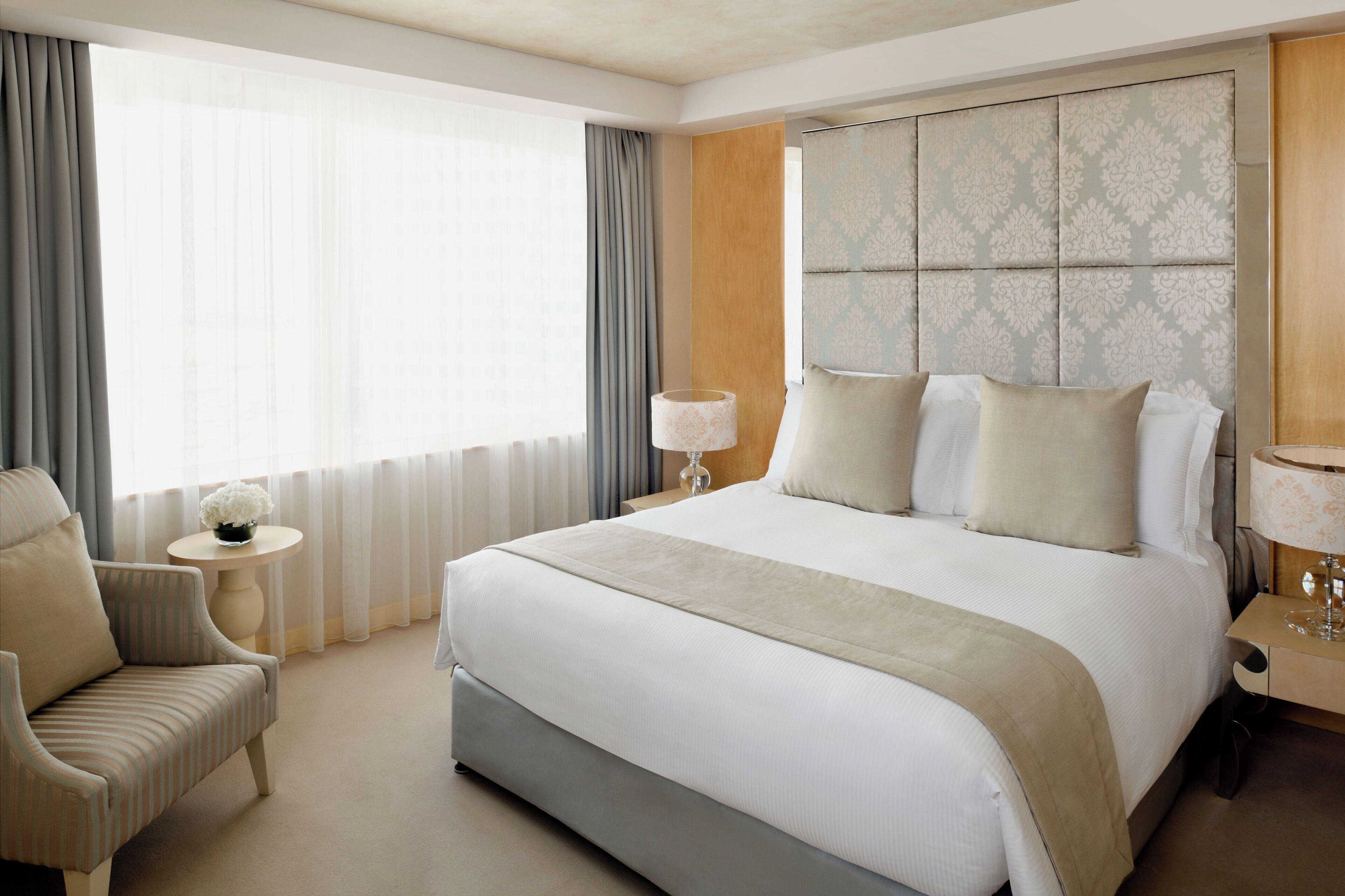 A hotel room with a large bed, a bedside table, a chair, and a view of the outdoors.