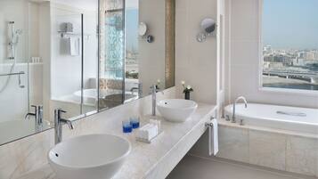 A modern bathroom with a large mirror, two sinks, a bathtub, and a city view.