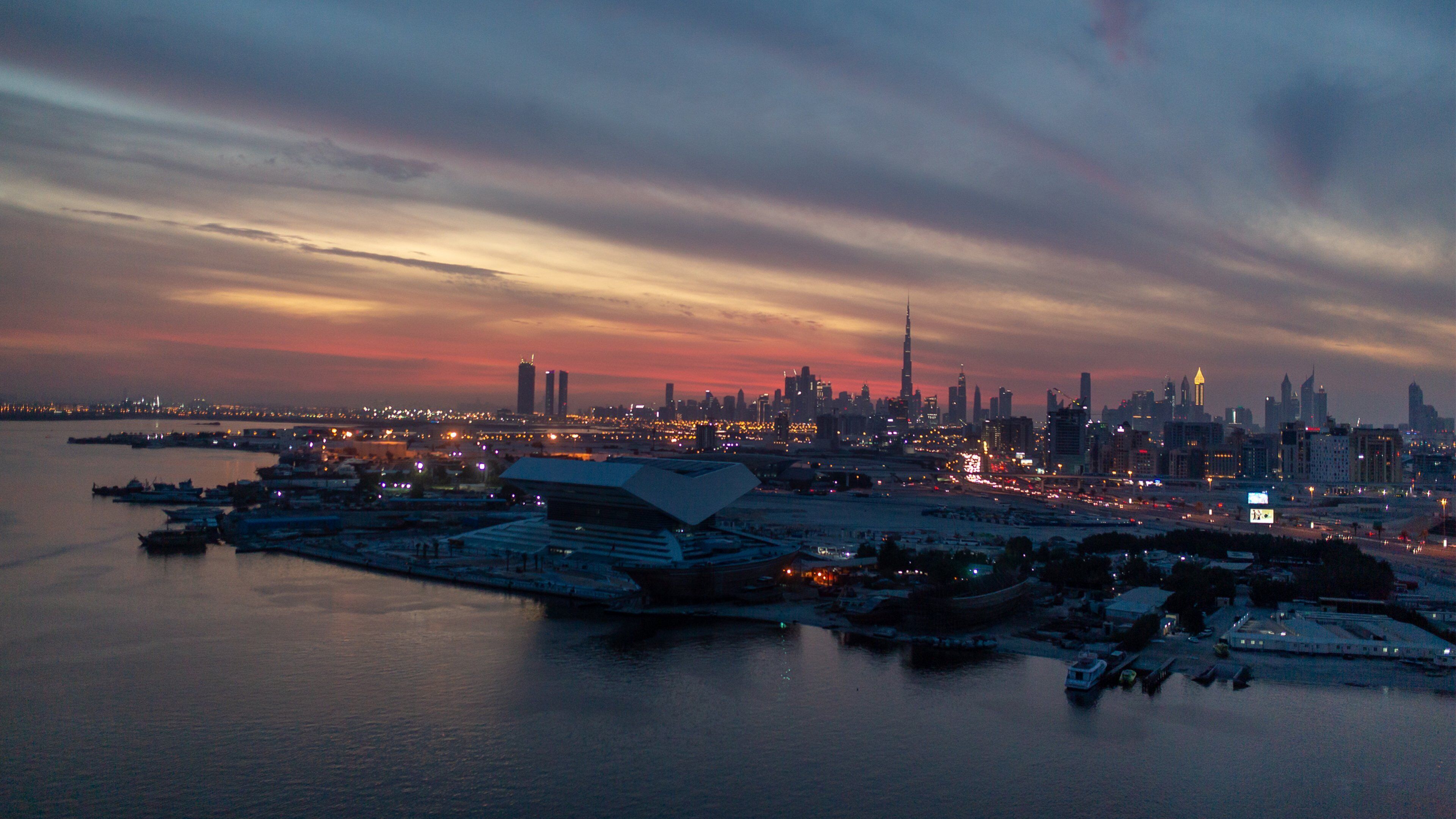 A city skyline at dusk with prominent skyscrapers, including a tall, uniquely shaped building near a waterfront.