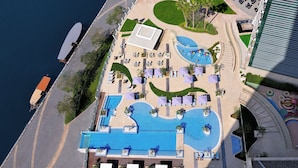 An aerial view of a resort with a large swimming pool, sun loungers, and a small beach area. - Crowne Plaza Festival City by IHG (Dubai)