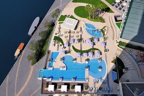 Ein Luftbild eines Resorts mit großem Pool, Liegestühlen und einer kleinen Strandbucht.