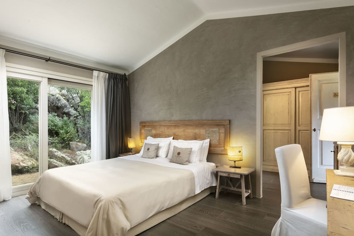 A spacious bedroom with a large bed, a nightstand, a chair, and a view of the outdoors.