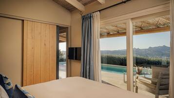 Une chambre avec un grand lit, une télévision et une vue sur une piscine et des montagnes.