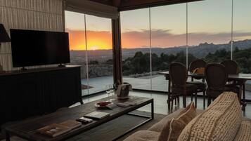 A modern living room with a flat-screen TV, a sofa, a coffee table, and a dining area with chairs.