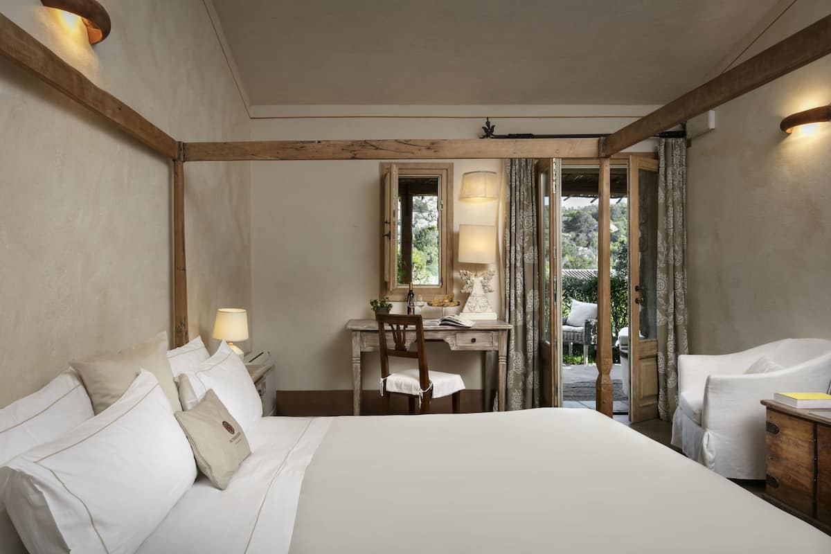 A hotel room with a large bed, a desk with a chair, a lamp, and a view through a glass door.