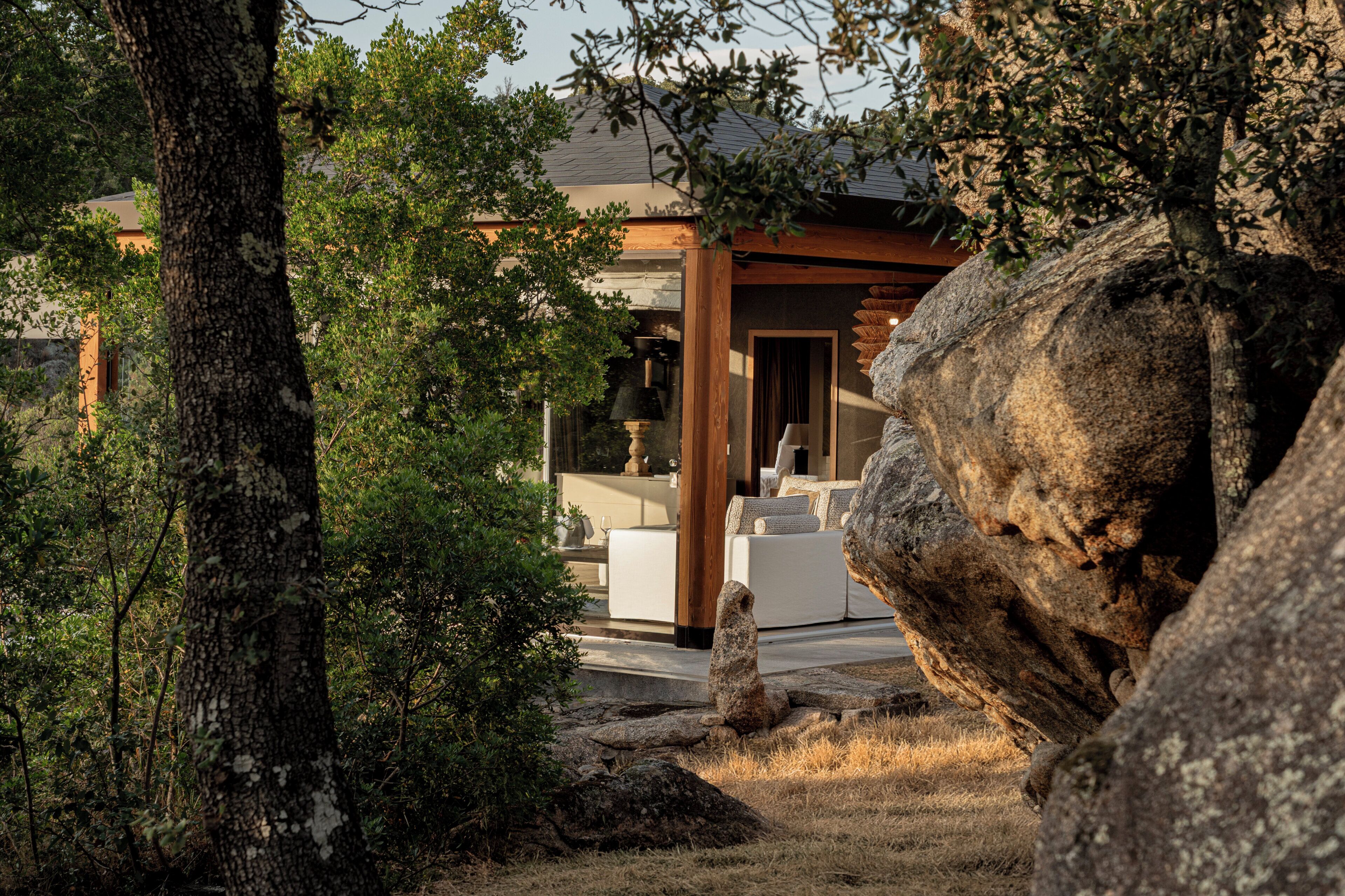 Un edificio moderno con fachada de piedra, una gran roca al frente y un área de estar exterior con muebles blancos.