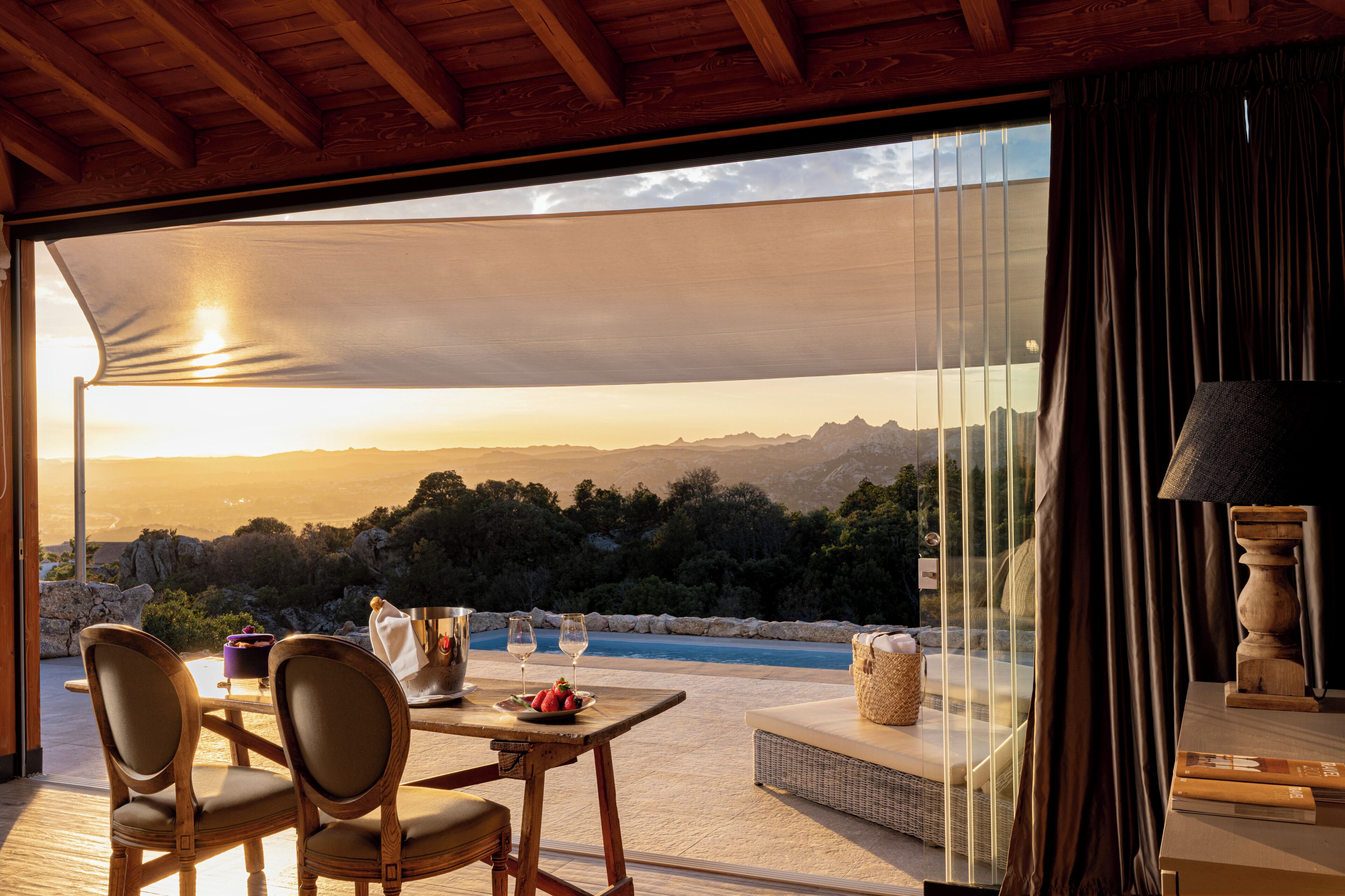A terrace with a table, chairs, a view of the mountains, and a pool.