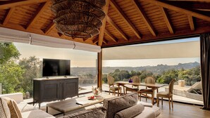Un vaste espace de vie doté d’un grand téléviseur, de meubles en bois et d’un coin repas offrant une vue sur un paysage montagneux.