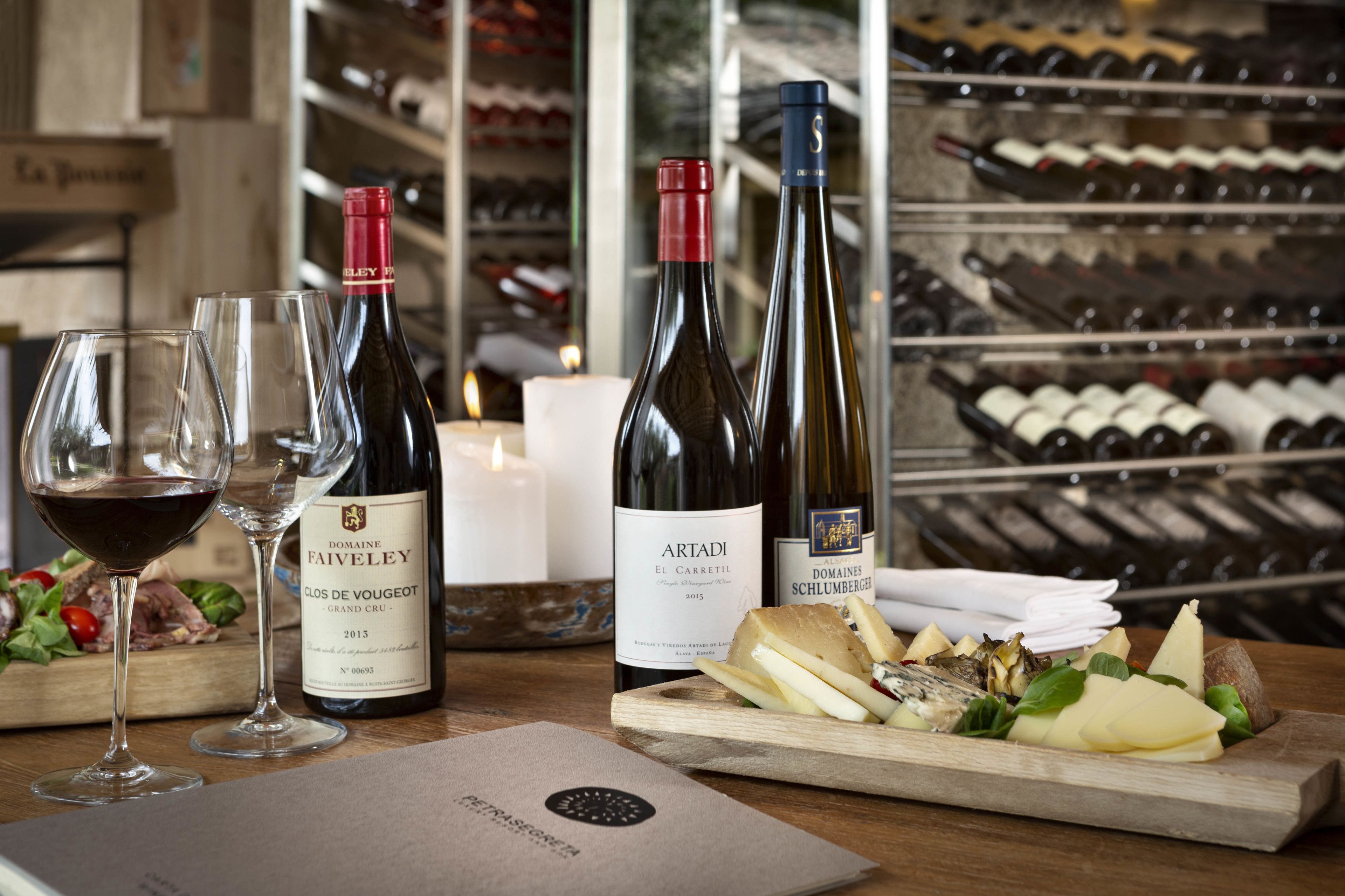 A wine tasting setup with bottles and glasses on a wooden table, a menu, and a wine rack in the background.