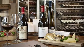 A wine tasting setup with bottles and glasses on a wooden table, a menu, and a wine rack in the background.